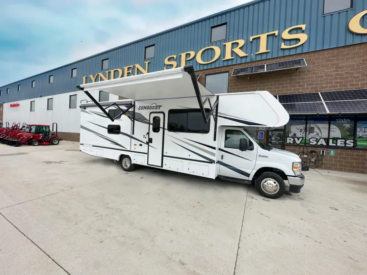 White Conquest RV with extended awning at Lynden Sports & RV Sales. Great for exploring RV rental options. Mahindra tractors are visible.. Gulf Stream Conquest 2023