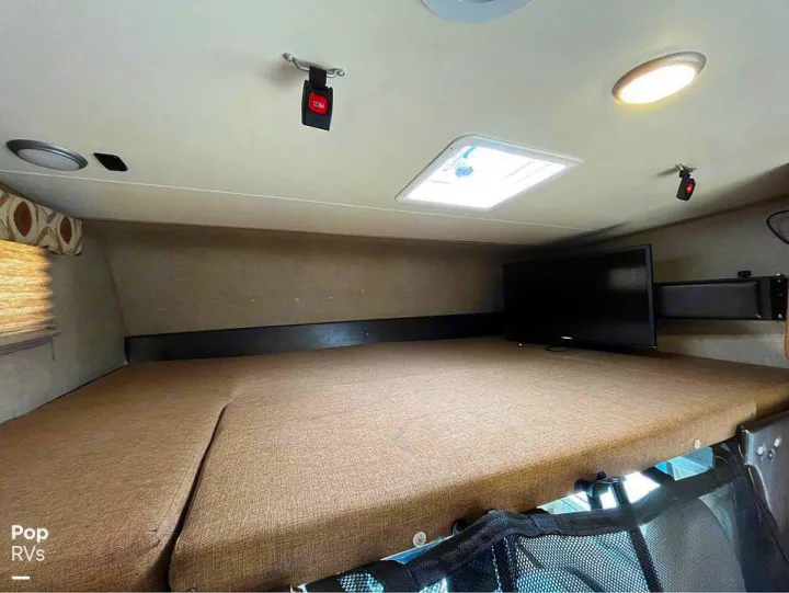 Spacious RV rental overhead bed area with a TV, skylight, and safety straps for a comfortable stay.. Coachmen Leprechaun 2015