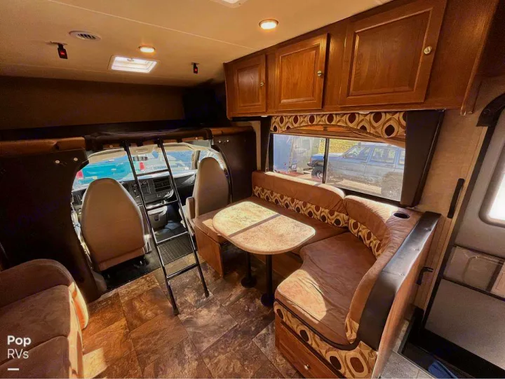 Inside an RV rental: a cozy dinette with patterned cushions, overhead bunk access ladder, and front cabin view.. Coachmen Leprechaun 2015