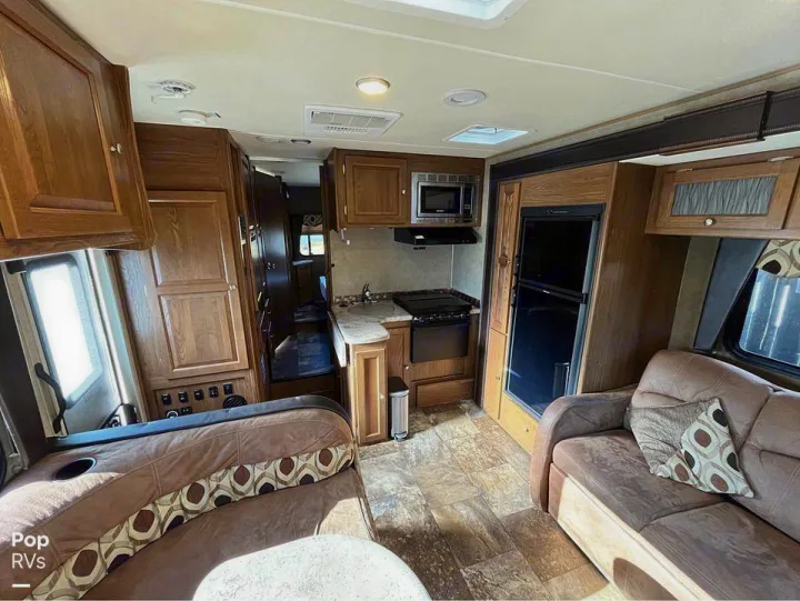 Well-appointed RV rental interior: kitchen with appliances, comfortable living space with sofas, and wood cabinetry.. Coachmen Leprechaun 2015
