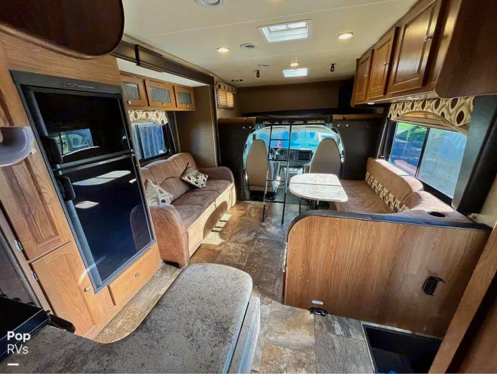 Cozy RV rental interior with a spacious living area, sofa, dinette, and forward bunk over the cab.. Coachmen Leprechaun 2015