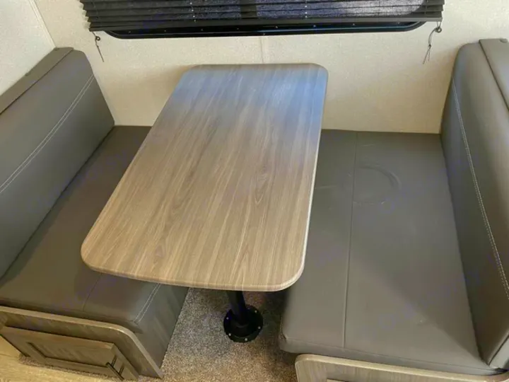 RV rental dinette with dark grey seats and wood-grain table, ideal for meals or bed conversion.. Forest River Shasta 2021