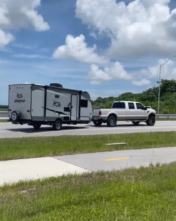 Sunny day drive! A large truck tows a Jayco RV travel trailer on the road, hinting at an ideal RV rental trip.. Jayco Jay Flight 2021