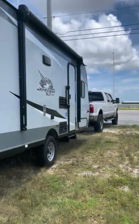 White Jay Flight SLX travel trailer, perfect for an rv rental, being towed by a pickup truck. Parked roadside on grass.. Jayco Jay Flight 2021