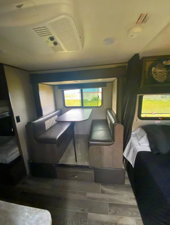 This RV rental interior features a dinette, bedroom, and bunk beds, with an overhead AC unit and wood-look floors.. Jayco Jay Flight 2021