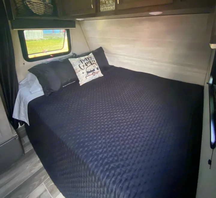 Comfortable RV rental sleeping area featuring a plush bed with dark bedding and a fun "Happy Camper" pillow.. Jayco Jay Flight 2021