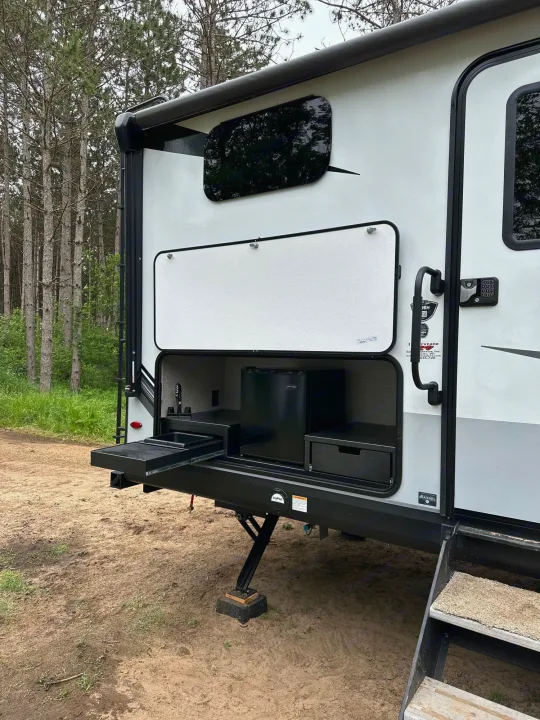 This RV rental's side compartment reveals an outdoor kitchen with a mini-fridge and pull-out sink, ideal for camping.. Jayco Whitehawk 2023