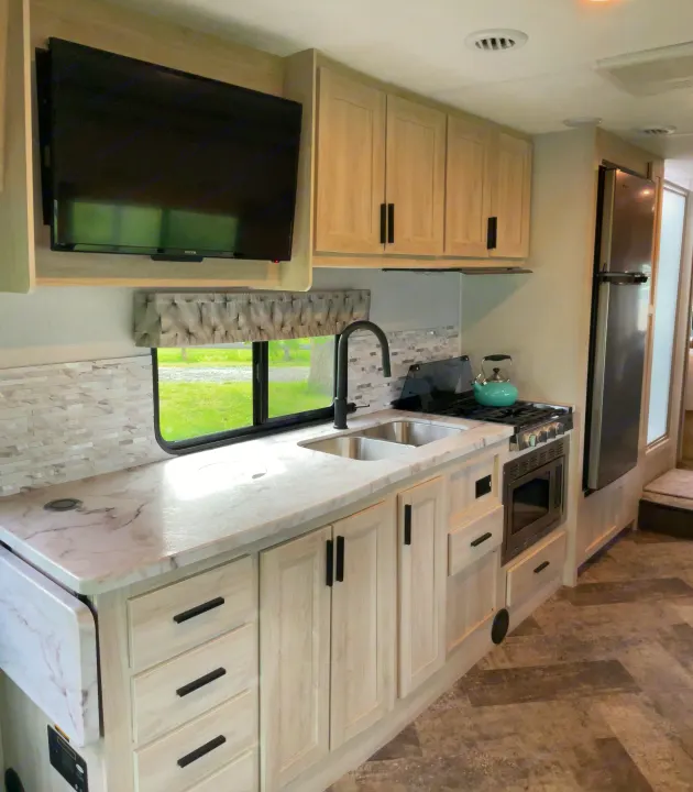 Modern RV rental kitchen interior featuring light cabinets, white marble countertop, and stainless steel appliances.. Forest River Sunseeker 2020