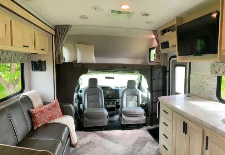 Spacious and modern RV rental interior featuring a living area, kitchen, overhead bunk, and front driving seats.. Forest River Sunseeker 2020
