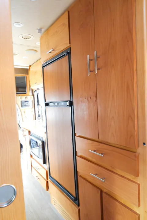 Explore this well-appointed RV rental interior, featuring a compact kitchen with wooden cabinets, refrigerator, and microwave.. Wayfarer Wayfarer Motorhome 2017