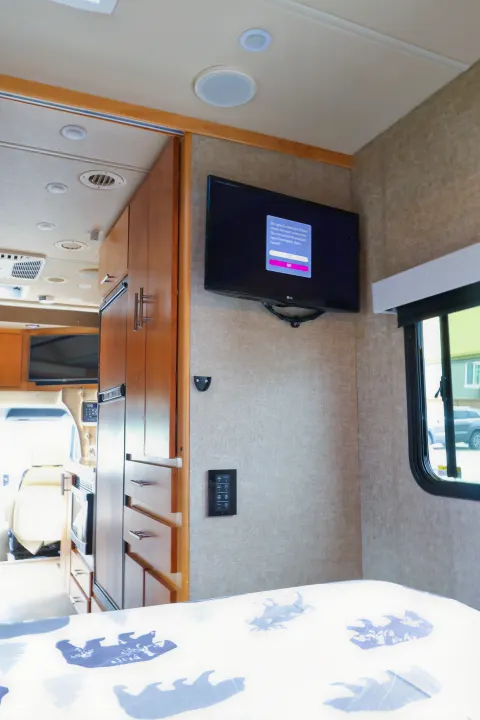 Interior of an RV rental bedroom featuring a TV with no signal, wood cabinetry, ceiling vents, and a patterned bed.. Wayfarer Wayfarer Motorhome 2017