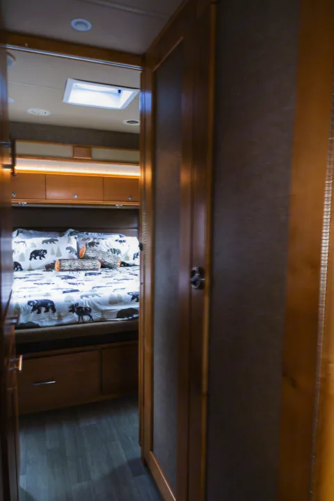Cozy RV rental bedroom with nature-themed bedding, overhead storage, and warm lighting, viewed through an open doorway.. Wayfarer Wayfarer Motorhome 2017