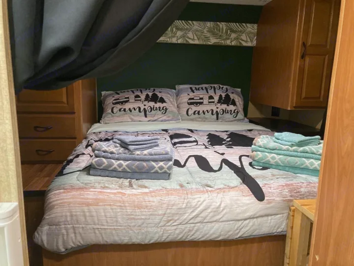Cozy RV rental bedroom with "Happy Camping" pillows and neatly folded towels, perfect for your next adventure.. Thor Majestic 2016