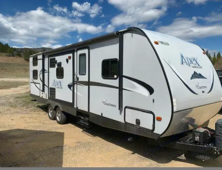 A white Coachmen Apex travel trailer, ready for your RV rental journey, parked on gravel under a cloudy sky.. Coachmen Apex 2015