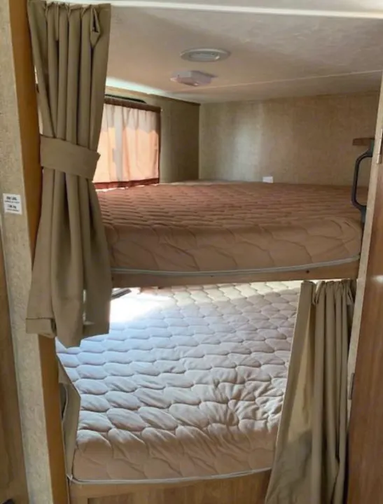 RV rental bunk room: Features two stacked bunk beds with light brown mattresses and tied-back curtains in a compact RV sleeping area.. Coachmen Apex 2015