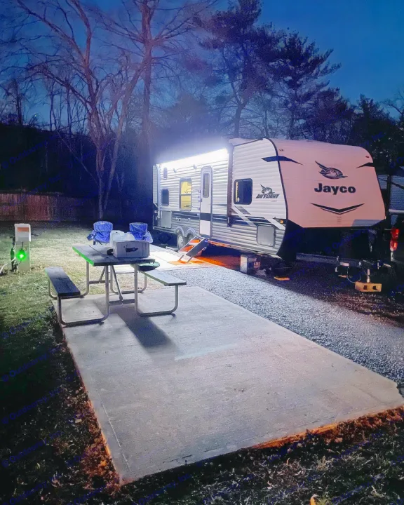 Night view of an illuminated Jayco RV rental parked at a campsite with a picnic table, chairs, and utility hookup.. Jayco Jay Flight SLX 2022