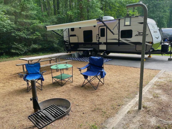 Serene RV rental campsite featuring a travel trailer with extended awning, picnic table, chairs, and a fire pit setup.. Jayco Jay Flight SLX 2022
