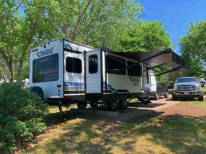 Spacious Vibe travel trailer RV rental at a sunny campsite, ready for relaxation with its extended slide-out & awning.. Forest River Vibe 2023