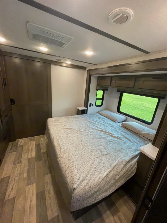 RV rental bedroom: a modern space with a large bed, patterned comforter, windows showing green landscape, and wood-look flooring.. FR3 FR3 Motorhome 2023