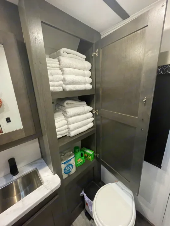 RV rental bathroom with organized storage, fresh towels, RV toilet paper, cleaning supplies, sink, and toilet.. FR3 FR3 Motorhome 2023