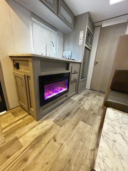 Modern RV rental interior featuring a kitchen with a sink, microwave, electric fireplace, and dinette seating.. Dutchmen Coleman Lantern LT 2022