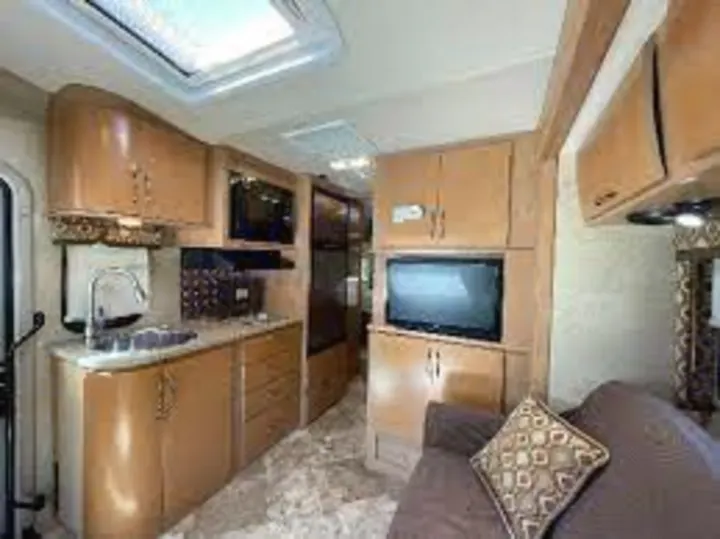 RV rental interior: compact kitchen with sink, microwave, and light wood cabinets, plus a living area with a TV and couch.. Thor Citation 2015