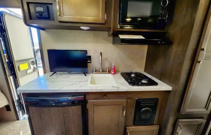 Inside our RV rental, a complete galley awaits: compact kitchen with sink, stove, microwave, fridge, and TV.. Jayco Jay Flight SLX 2020