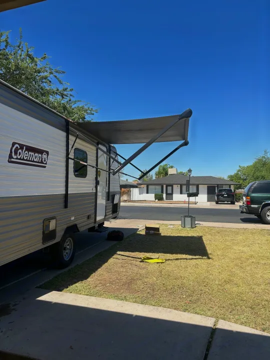 Coleman travel trailer RV rental with awning extended, parked in a sunny driveway. House visible across the street.. Coleman Lantern LT 17B 2023