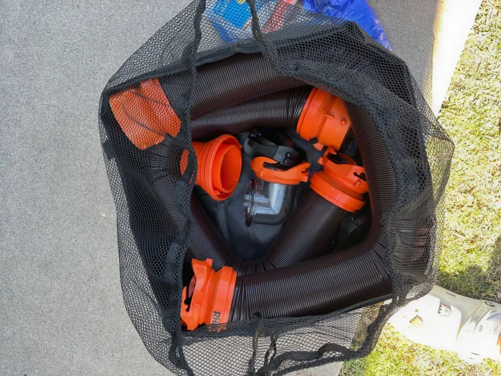 RV rental essential: Black corrugated sewer hoses and orange fittings visible in a mesh bag, ready for setup.. Coleman Lantern LT 17B 2023