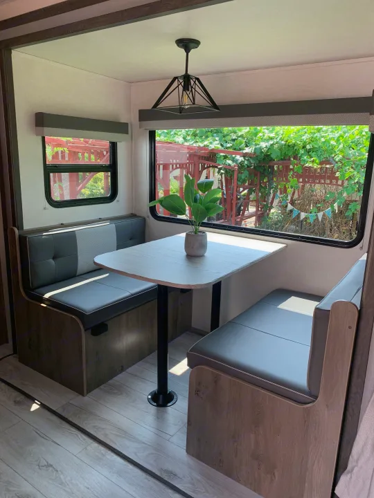 Modern RV rental dinette with cozy benches, light wood table, and ambient light, offering a view of lush greenery.. Forest River Surveyor Legend 2022