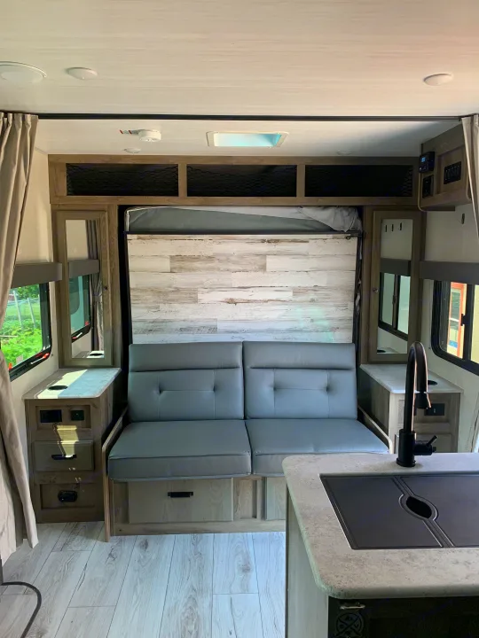 RV rental interior: modern kitchen, gray dinette seating, and bed area on light wood-look flooring.. Forest River Surveyor Legend 2022