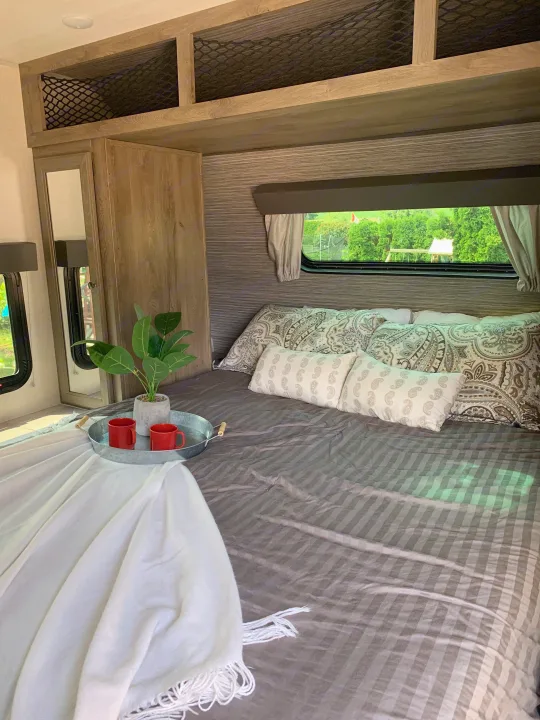 Cozy rv rental bedroom interior with patterned bed, green view from window, and smart storage for a relaxing stay.. Forest River Surveyor Legend 2022