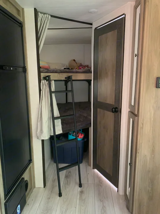RV rental bunk beds with a ladder, overhead storage cabinets, and light-colored interior finishes.. Forest River Surveyor Legend 2022