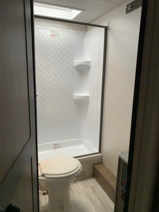 An RV rental bathroom interior, featuring a white toilet on the right and a shower with white herringbone and subway tiles. View from above.. Forest River Surveyor Legend 2022