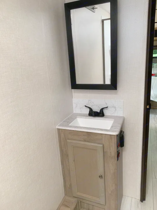 RV rental bathroom: Modern wood-grain vanity, white sink, black faucet, tiled backsplash, and mirror.. Forest River Surveyor Legend 2022