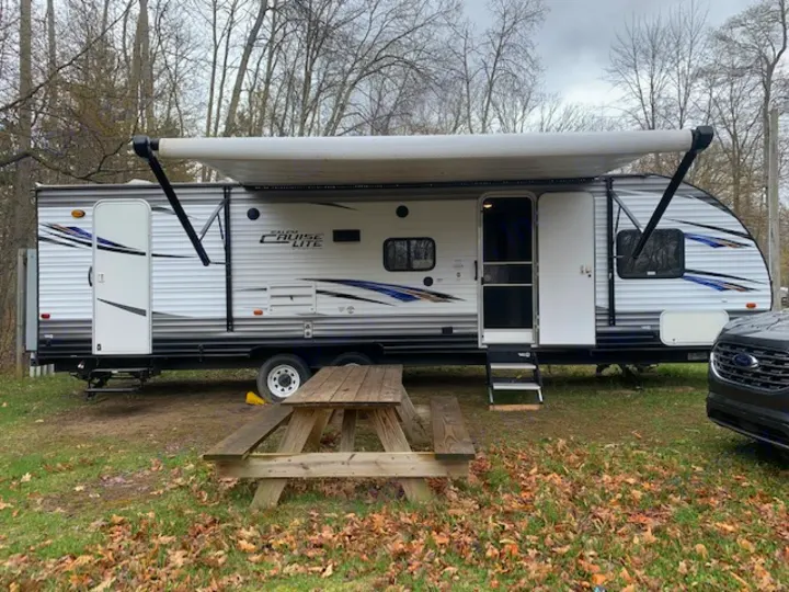 This rv rental, a white travel trailer with an extended awning, is parked at a grassy campsite with a wooden picnic table.. Forest River Salem Cruise Lite 2018