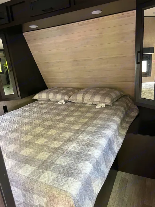 Inviting RV rental bedroom with a grey checkered comforter, light wood paneling, and dark built-in storage.. Jayco Jay Flight 2022