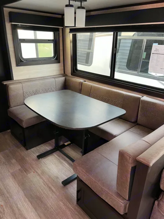 RV rental interior: inviting L-shaped dinette with table & windows. Gray upholstery, dark wood accents.. Jayco Jay Flight 2022