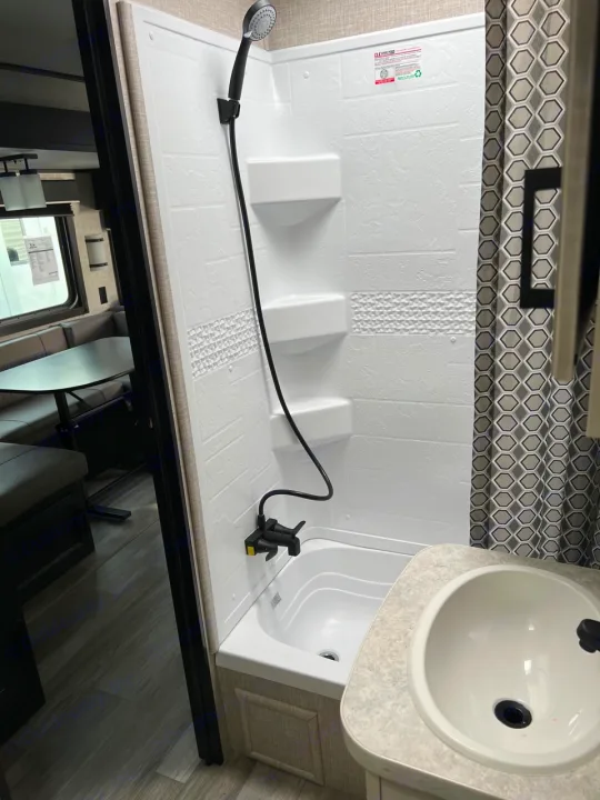 RV rental bathroom features a white shower stall with handheld showerhead and compact sink.. Jayco Jay Flight 2022