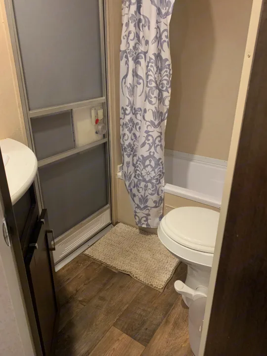 A compact RV rental bathroom: toilet, tub/shower with grey patterned curtain, sink, and wood-look floor. Perfect for travel.. Forest River Salem Cruise Lite 2018