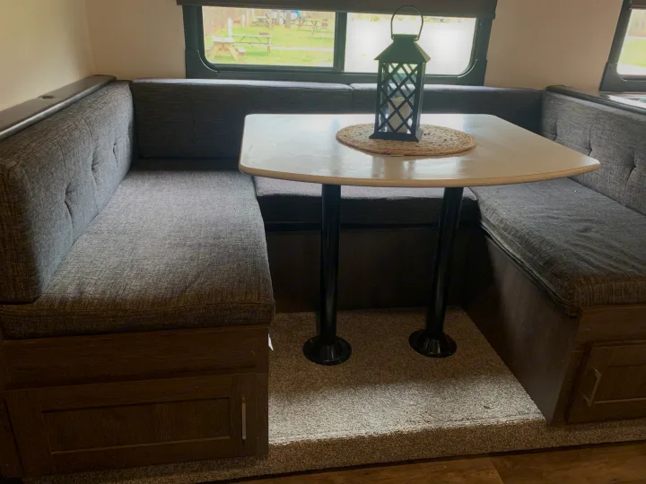 Inside an RV rental: a comfortable gray dinette with a white table, lantern, and scenic window view.. Forest River Salem Cruise Lite 2018
