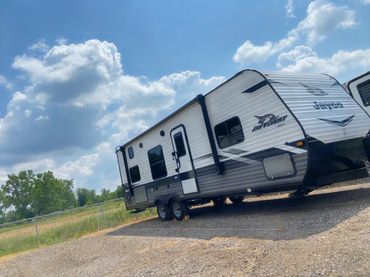 This white and grey Jayco Jay Flight RV rental, a travel trailer, is parked on a gravel lot under a blue sky with white clouds.. Jayco Jay Flight SLX 2022