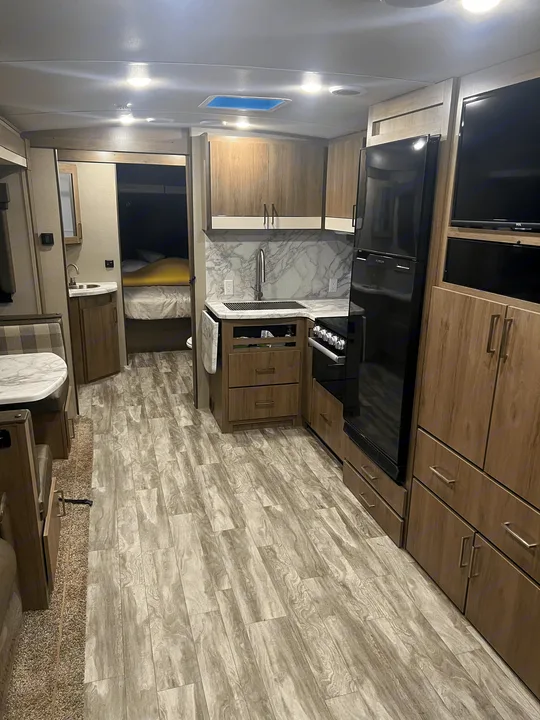 Modern RV rental interior with a functional kitchen, dining area, and glimpse of bunk beds, offering a complete living space.. Grand Design Imagine 2022