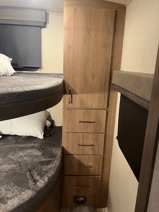 RV rental interior: stacked bunk beds with grey bedding, wood-look cabinet with drawers, and window blinds.. Grand Design Imagine 2022