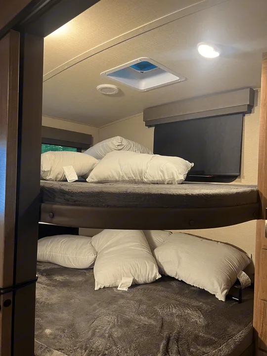 Cozy RV rental bunk beds with striped pillows, dark blankets, & a window for comfortable sleep.. Grand Design Imagine 2022