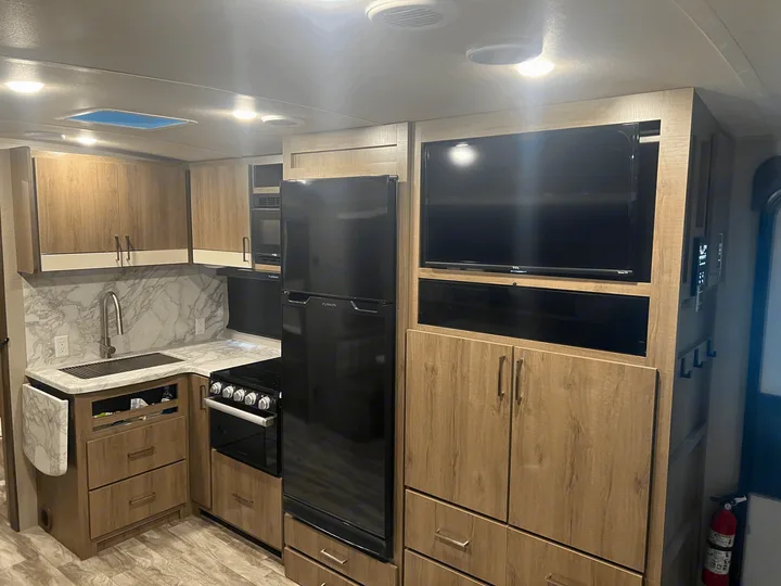 Modern RV rental interior with full kitchen, TV, and ample storage, featuring light wood cabinetry.. Grand Design Imagine 2022