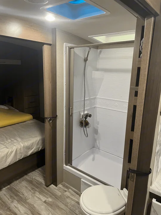 Compact RV rental interior with a practical bathroom (shower, toilet) and cozy bedroom, optimized for travel comfort.. Grand Design Imagine 2022