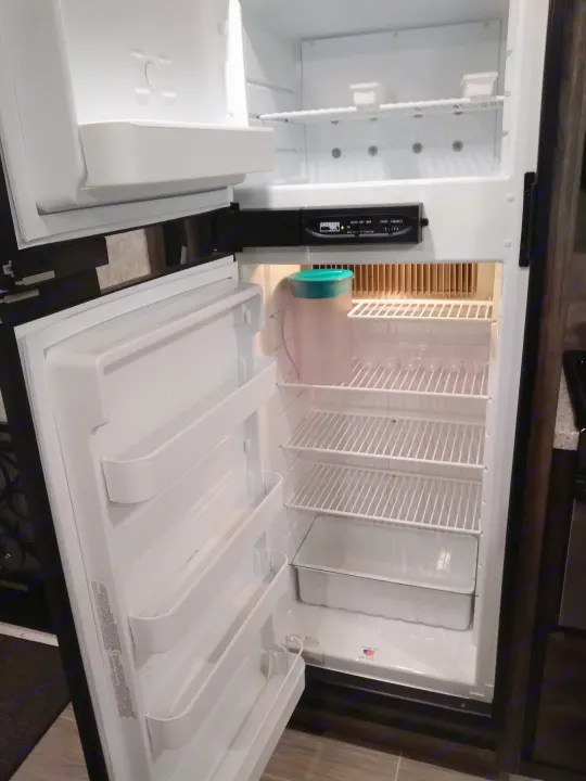 Inside an RV rental, an open, empty refrigerator and freezer reveal wire shelves, door bins, and a control panel.. Highland Ridge RV Open Range Ultra Lite 2018
