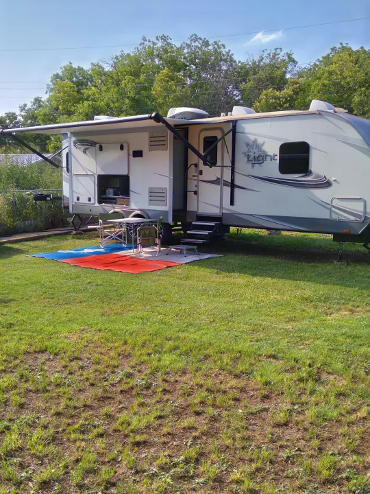 RV rental at a sunny campsite, featuring an extended awning, outdoor seating, and grill setup.. Highland Ridge RV Open Range Ultra Lite 2018