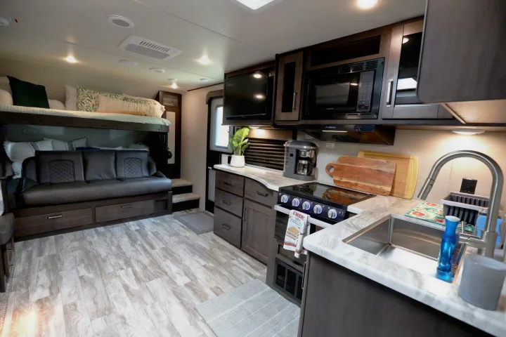 Bright RV rental interior featuring a practical kitchen with stove & sink, and a comfortable bunk bed/sofa living space.. Grand Design Transcend Xplor 2022